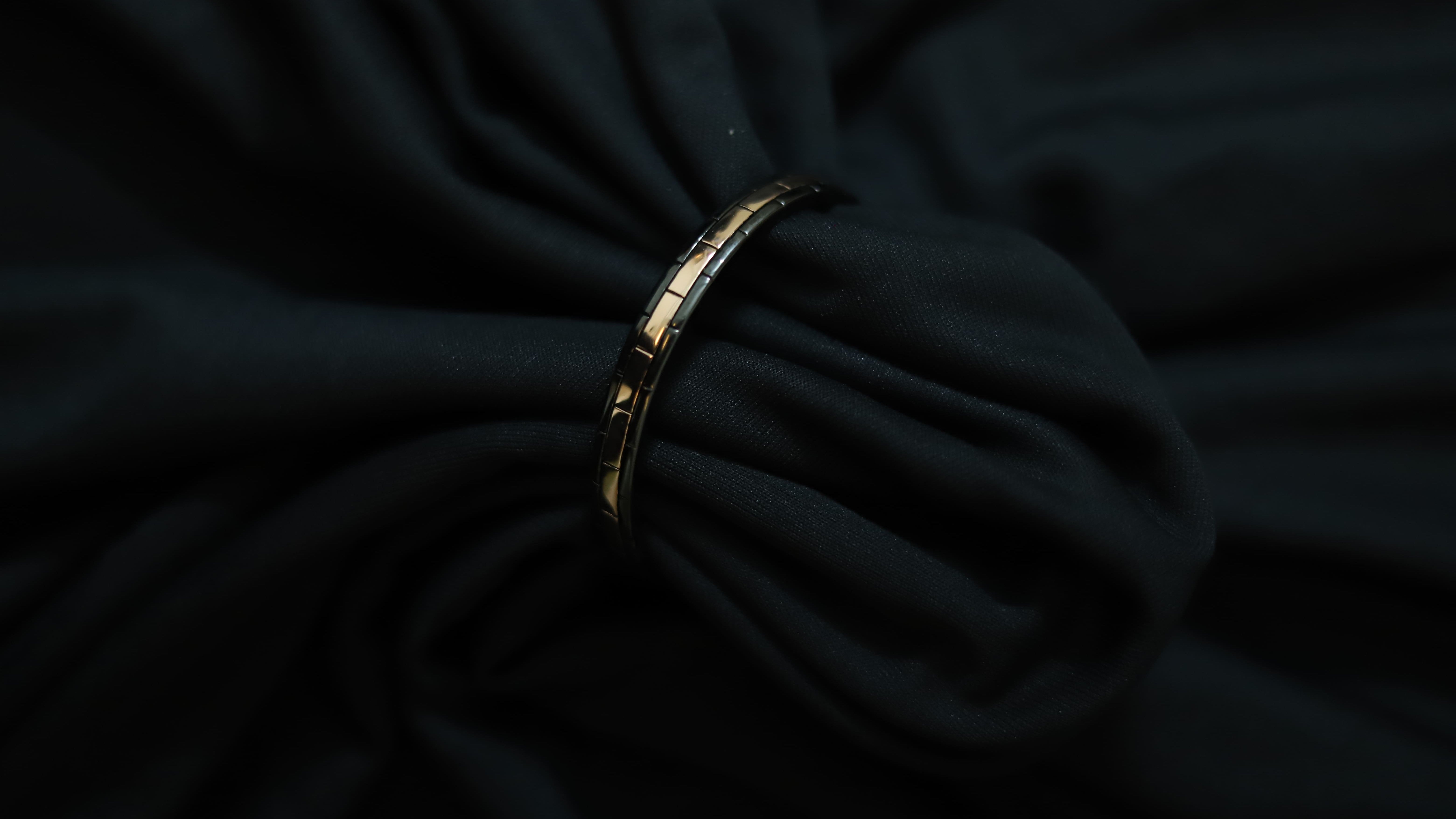 A gold-toned segmented bangle bracelet with black inlay details, shown resting on draped black fabric.
